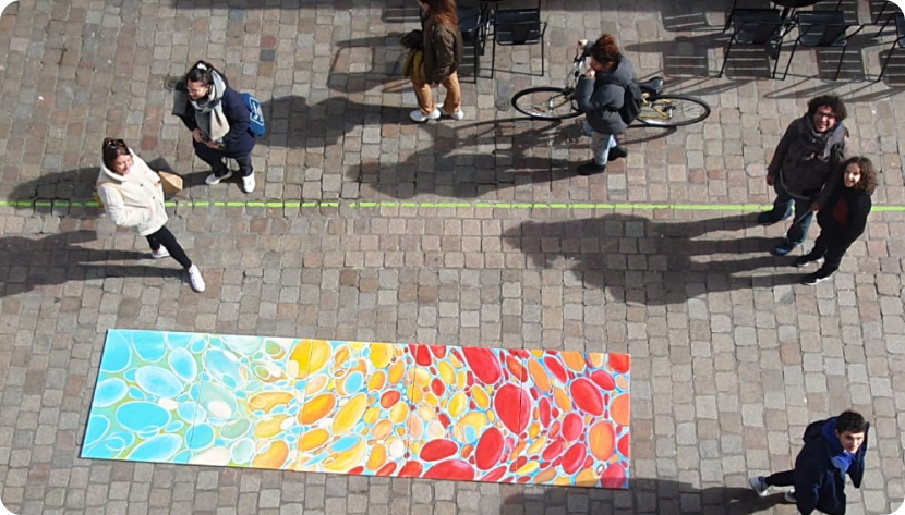 photo vue d'en haut. 
                        Diego et des passants devant un ensemble des peintures de bulles 
                        colorées exposés au sol dans la rue